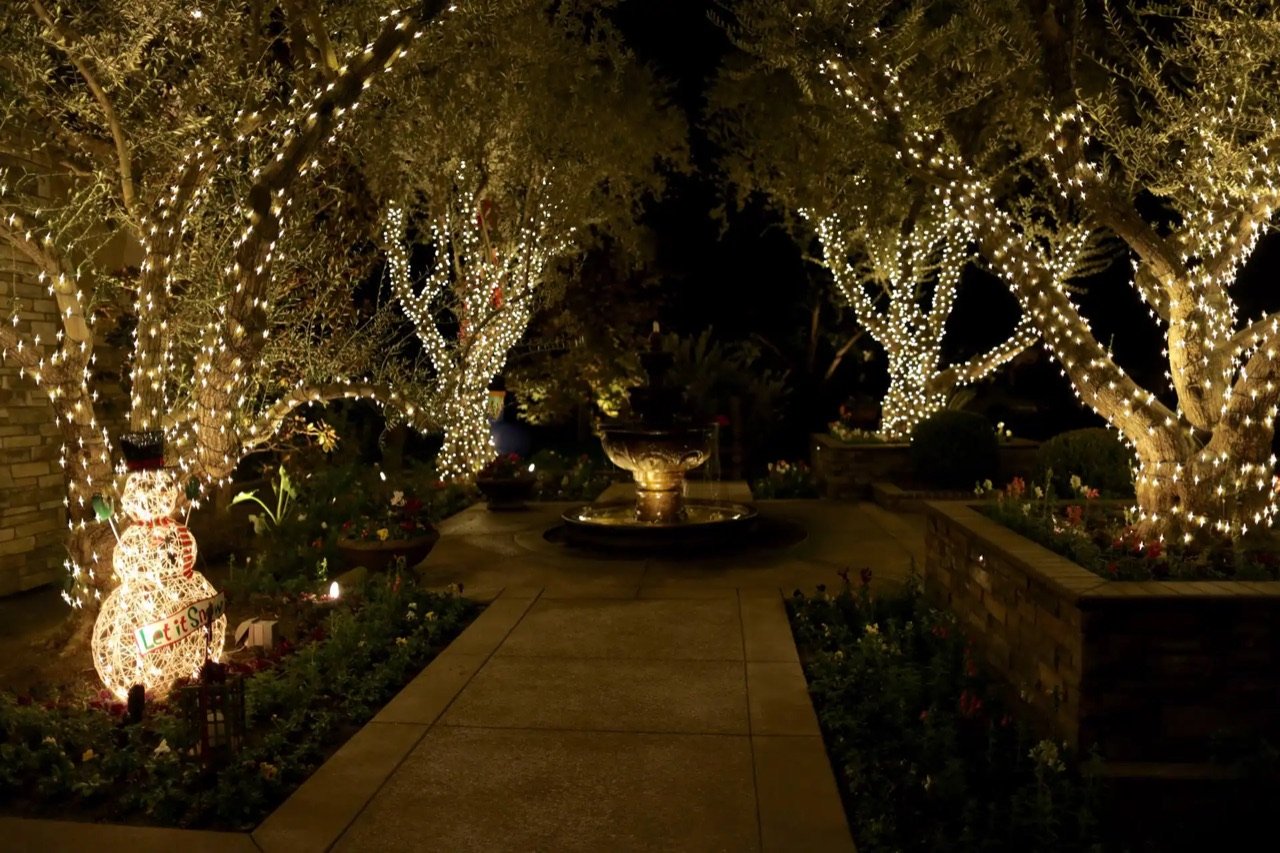 Christmas lights wrapped around courtyard trees with a lighted snowman display