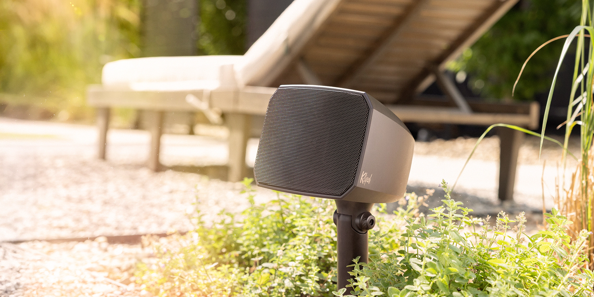 Low-profile landscape speaker installed near patio lounge seating