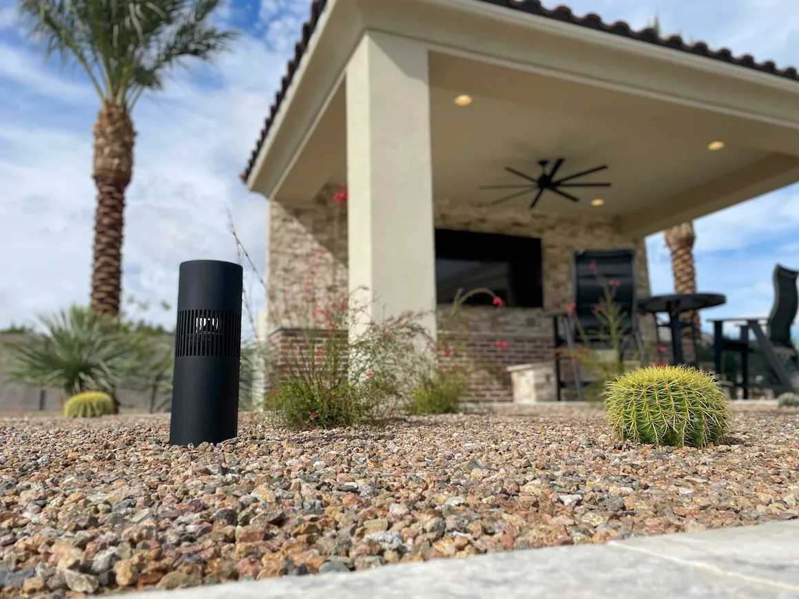 Black outdoor speaker installed in a gravel landscape bed near a covered patio